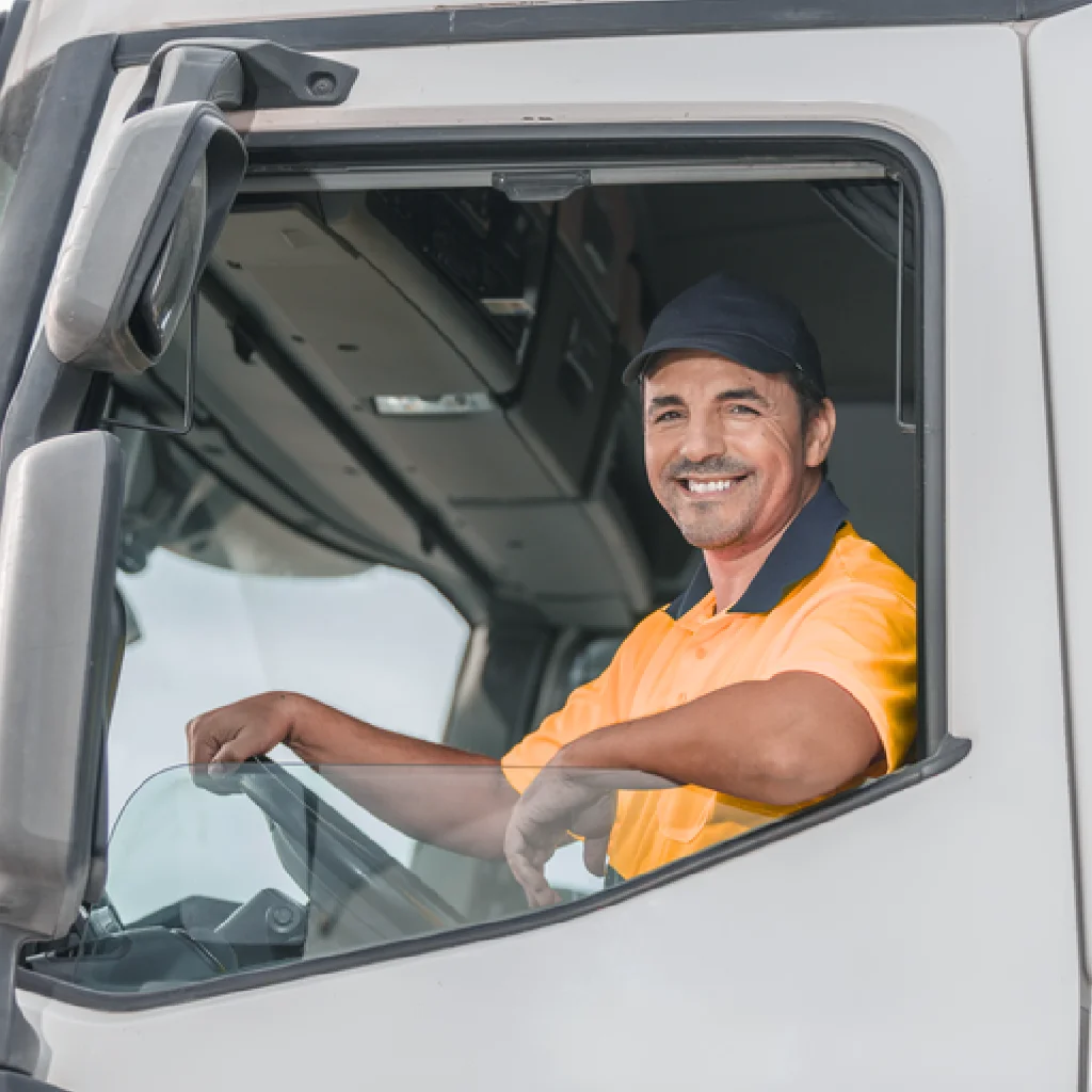 Rekrutierung von Berufskraftfahrern Ein Mann sitzt mit orangenen Hemd in einem weißen LKW und legt seinen Arm auf dem offenen Fenster ab und laechelt nach draussen
