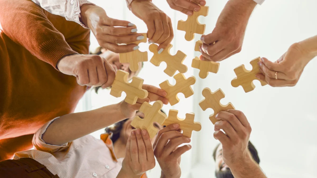 Mehrere Personen stehen in einem Kreis und halten jeweils ein Puzzelteil aus Holz in den Haenden 