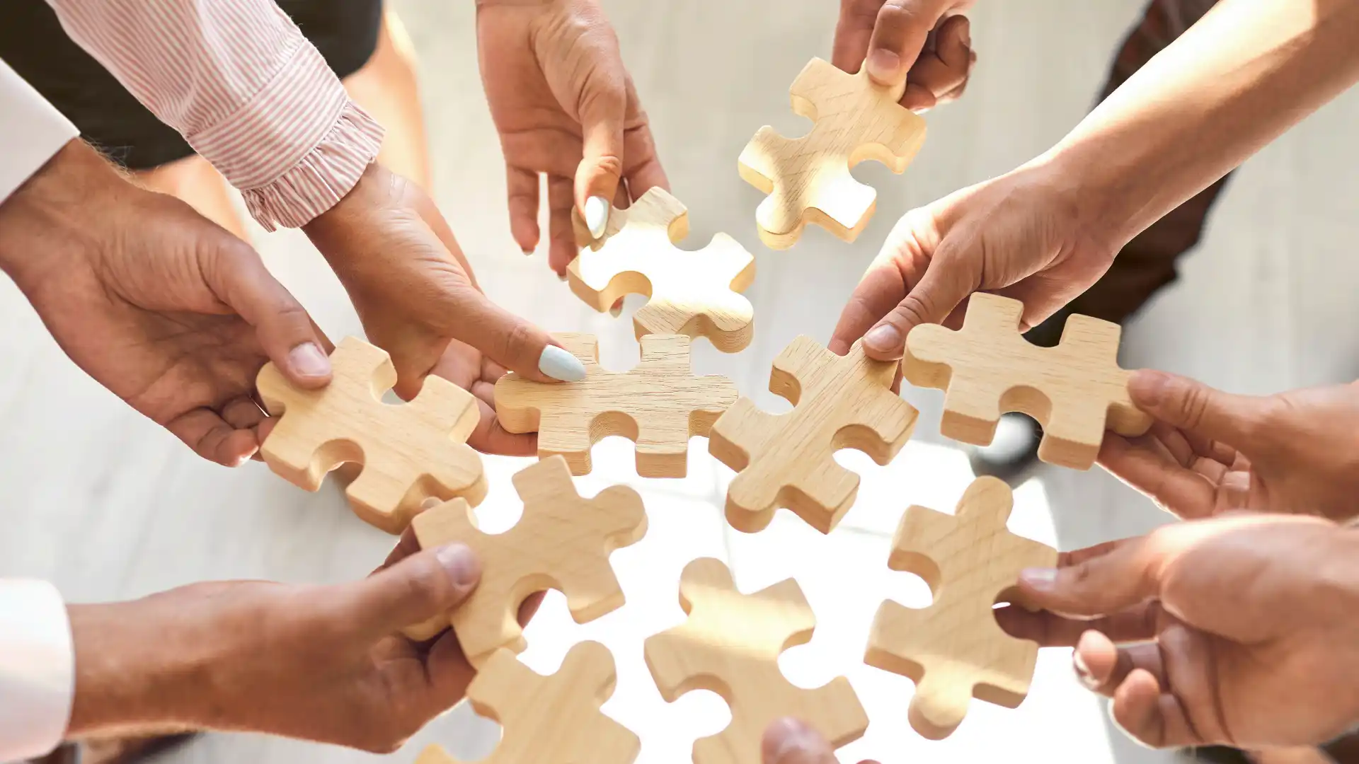 Mehrere Personen stehen in einem Kreis und halten jeweils ein Puzzelteil aus Holz in den Haenden 